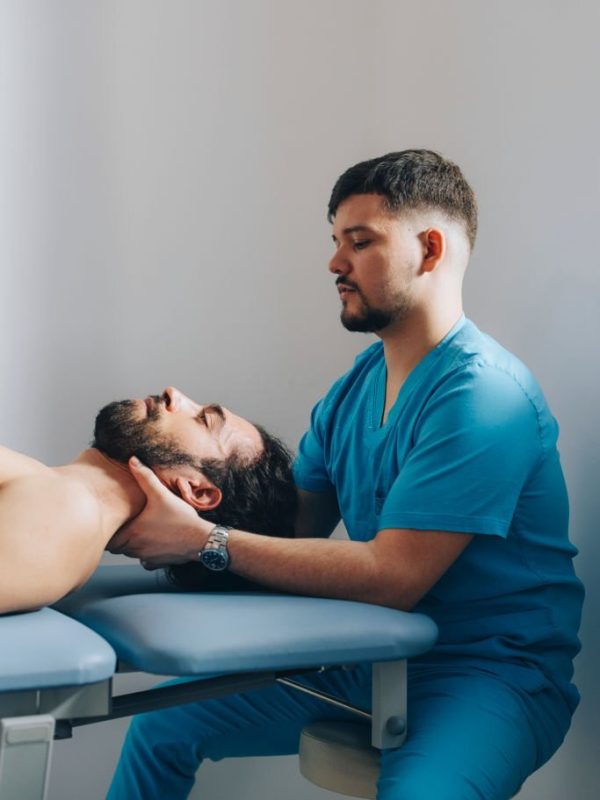 Patient is calmly lying on his back while the chiropractor is holding his neck, massaging it and adjusting it.